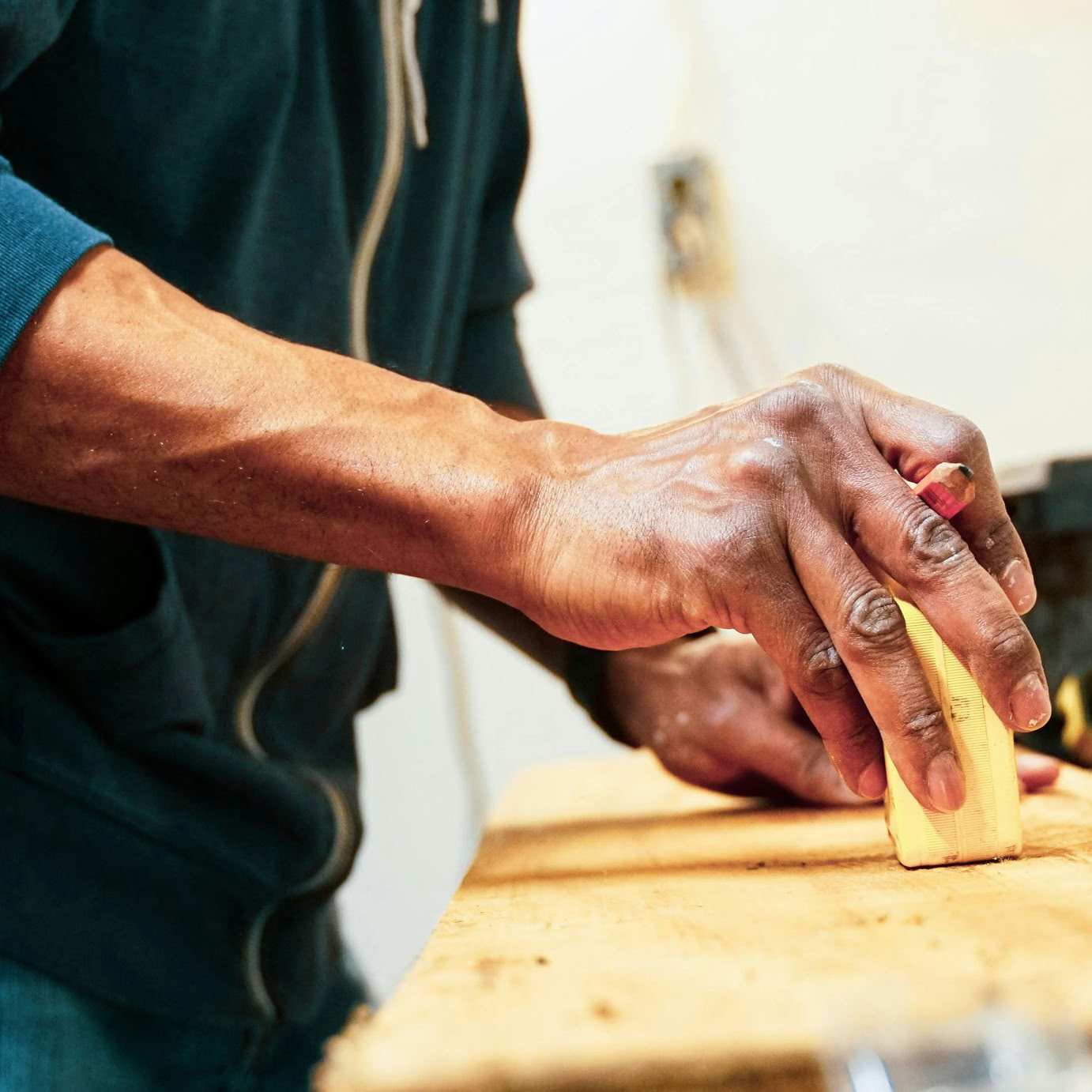 Detailed shot of a woodworker's hand sanding a wooden surface in a workshop setting.